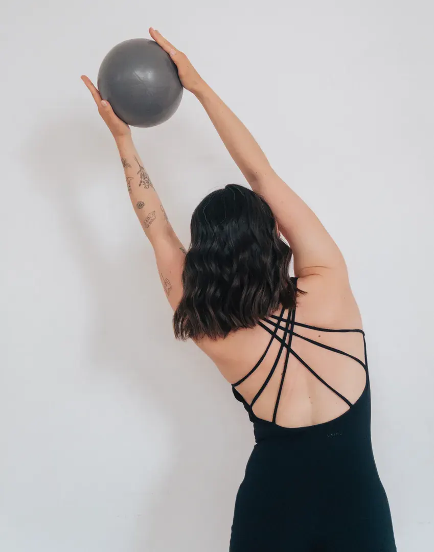 Trainerin dehnt sich mit einem Pilatesball über dem Kopf zur Seite