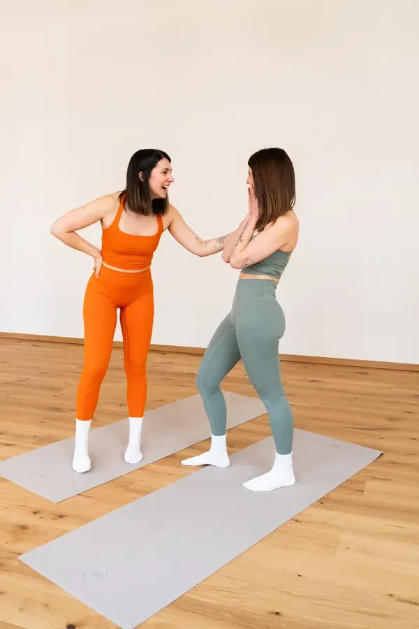 Zwei Trainerinnen lachen gemeinsam auf den Pilatesmatten im Studio